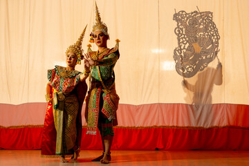 Obraz premium Two people of man and woman with Khon or Mask dance dress stand with performance action in front of grand shadow play in the background with white screen.