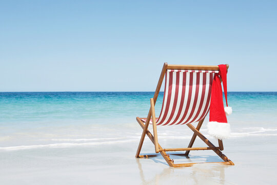 Red and white striped deck chair with Christmas hat by the sea. - Powered by Adobe