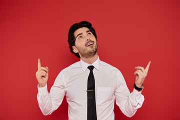 Young handsome man in white shirt and tie expressing joy against vibrant red background