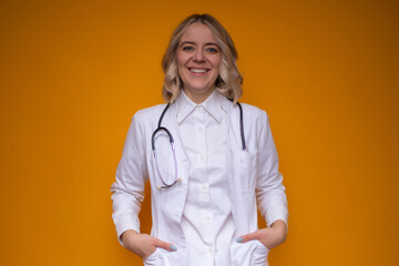 A smiling female doctor in a white lab coat with a stethoscope stands confidently against a vibrant yellow background, exuding professionalism, friendliness, and approachability.