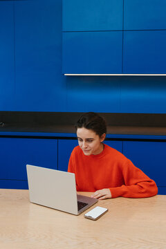 A woman uses a laptop sitting in the kitchen
