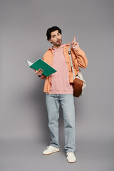 Handsome young man showcasing a lively expression while holding a notebook in a modern studio