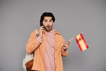 Young handsome man holds Spanish flag while talking on the phone in a casual indoor setting