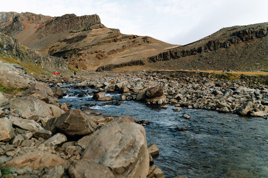 Wild river in rocky mountain valley with distant hikers.