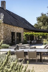 Outdoor dining area featuring a modern stone house surrounded by greenery on a sunny day in a tranquil countryside setting