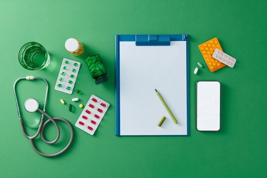 Colorful pills, stethoscope, clipboard on green background
