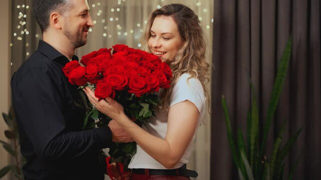 Romantic man gives a gift luxurious bouquet flowers red roses to beloved woman. Happy couple in love on Valentine's Day. guy comes on date with girl. night dark room. Smiling face joy family together