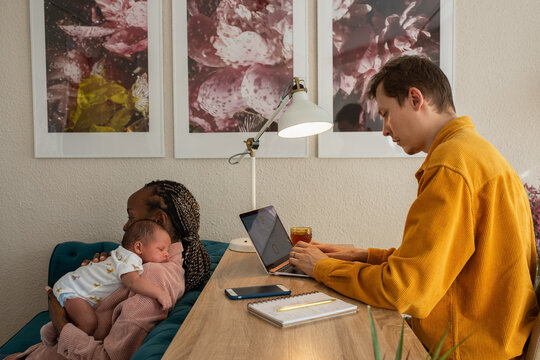 Mom holding baby to burp after feeding while father is working