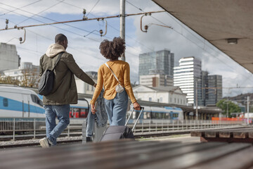 African American couple walking and carrying suitcases along a railway station, ready for their train travel. Traveler lifestyles concept.