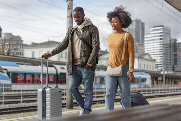 African American couple walking and carrying suitcases along a railway station, ready for their train travel. Traveler lifestyles concept.