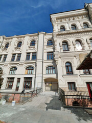 A historic neoclassical building with arched windows, intricate moldings, and a paved ramp leading to its entrance. The photo highlights accessibility within preserved architectural heritage.