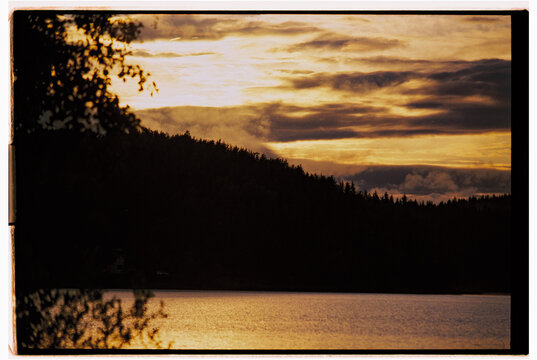 Sunset over tranquil lake surrounded by forested hills.