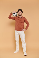 Fototapeta premium Handsome young man posing confidently with a soccer ball in a vibrant studio setting