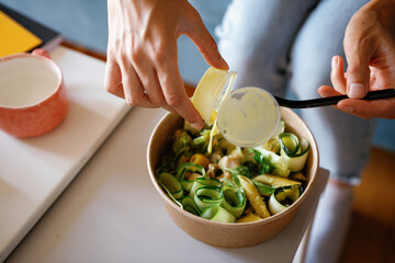 Top of partial woman pouring sauce in ripe salad in bowl at table