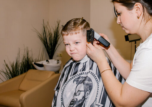 The boy is squirming while the barber cuts his hair.