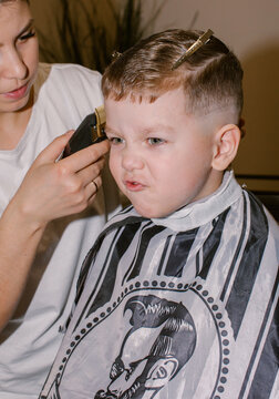The boy is squirming while the barber cuts his hair.