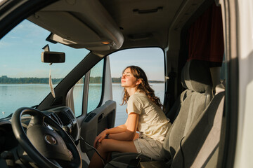 Woman sitting on seat of camper van during road trip in summer sunbath