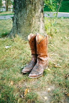Worn leather cowboy boots resting on green grass near a tree
