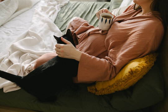 A pregnant woman with a cup of tea and her cat