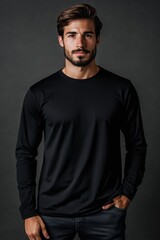 Obraz premium A confident young man with a well-groomed beard, wearing a black long sleeve T-shirt mockup, standing against a dark background. He has a serious expression and is posing with one hand in his pocket.