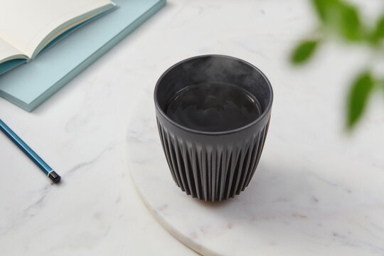 Drip coffee in black cup standing marble table near pen and books
