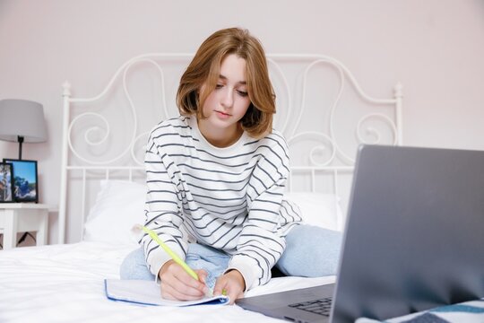 Young caucasian female school student writing in notebook at home