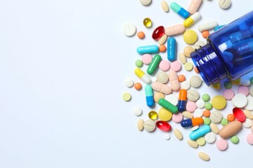Various pills pouring out of medicine bottle on white background