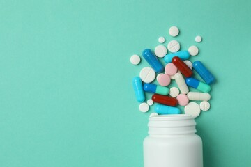 Various pills pouring out of medicine bottle on color background