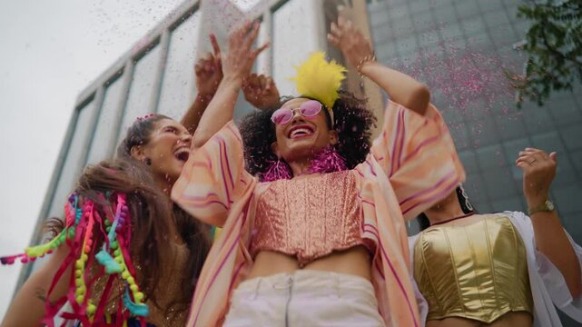 Joyful Woman Throwing Confetti and Dancing at Brazilian Carnival Street Party. Vibrant Group in Colorful Costumes Celebrating Carnaval Festivities in a Low Angle View