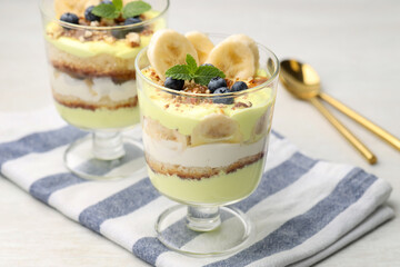 Tasty trifle dessert. Banana, blueberries, sponge cake and whipped cream in glasses on white wooden table