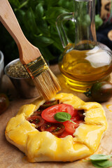 Putting egg yolk onto raw galette with tomato and basil on table, closeup