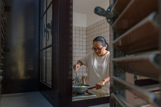 Indonesian woman cooking fried rice in the kitchen, window framing