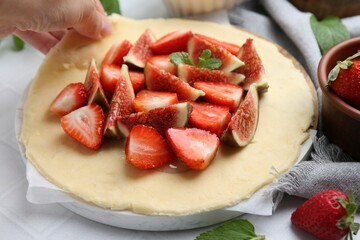 Woman making galette with strawberries and figs at light table, closeup
