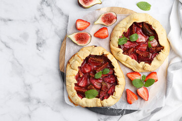 Tasty galettes with strawberries, figs and mint on white marble table, top view. Space for text