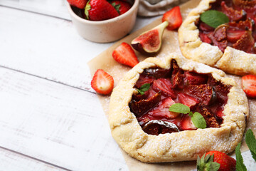 Tasty galettes with strawberries, figs and mint on wooden table, closeup