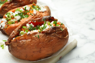 Tasty cooked sweet potatoes with feta cheese, green onion and parsley on white marble table, closeup