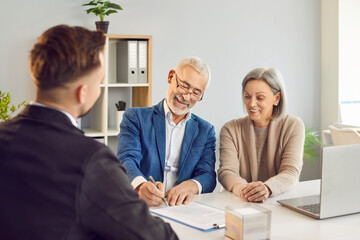 Happy senior couple clients is signing a contract with an real estate agent, financial adviser, or...
