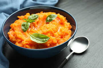 Tasty mashed sweet potato in bowl served on dark gray textured table, closeup