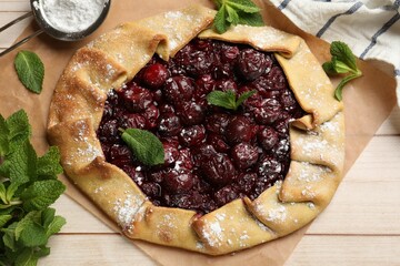 Tasty galette with cherries, mint and powdered sugar on wooden table, flat lay