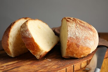 Cut loaf of fresh bread and knife on wooden table, closeup