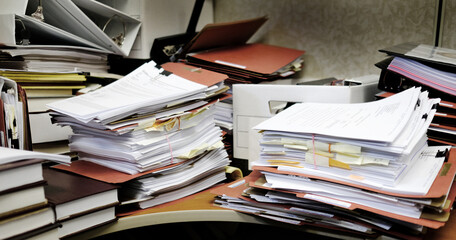 Messy Desk with Books Binders Files and Papers Stacked up High in a Disorganized Office Space