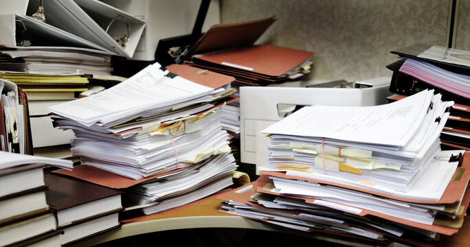 Messy Desk with Books Binders Files and Papers Stacked up High in a Disorganized Office Space