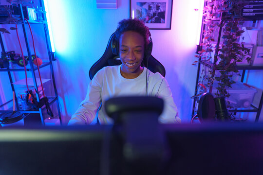 Smiling Teen Gamer at Desk in Neon-Lit Room