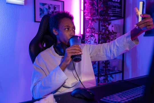 Young Man Taking Selfie While Drinking at Gaming Desk with Neon Light