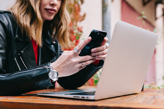 A young woman works on her laptop while using her smartphone