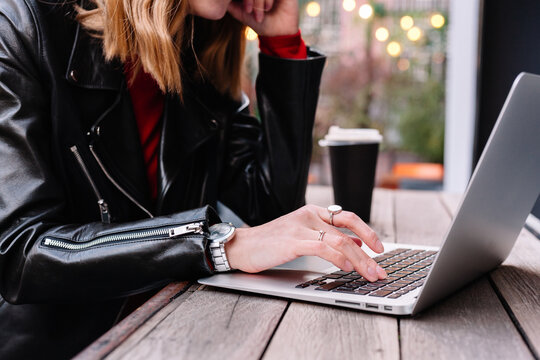 A young woman in a leather jacket works on a laptop closeup hands