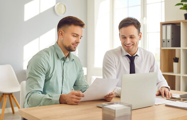 Two young confident smiling business people and company employees working in office at the desk...