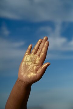 A golden hand reaching towards a bright blue sky