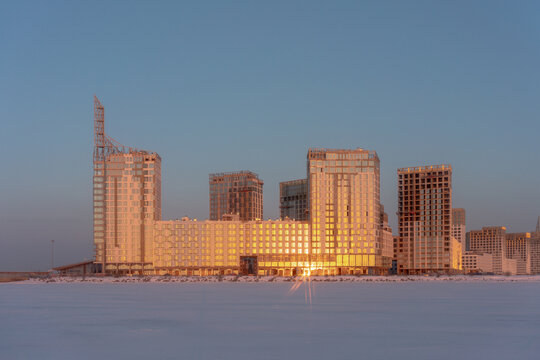 Modern construction site viewed from frozen bay at sunset