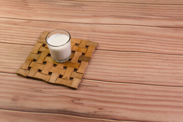 A glass of milk is sitting on a wooden coaster